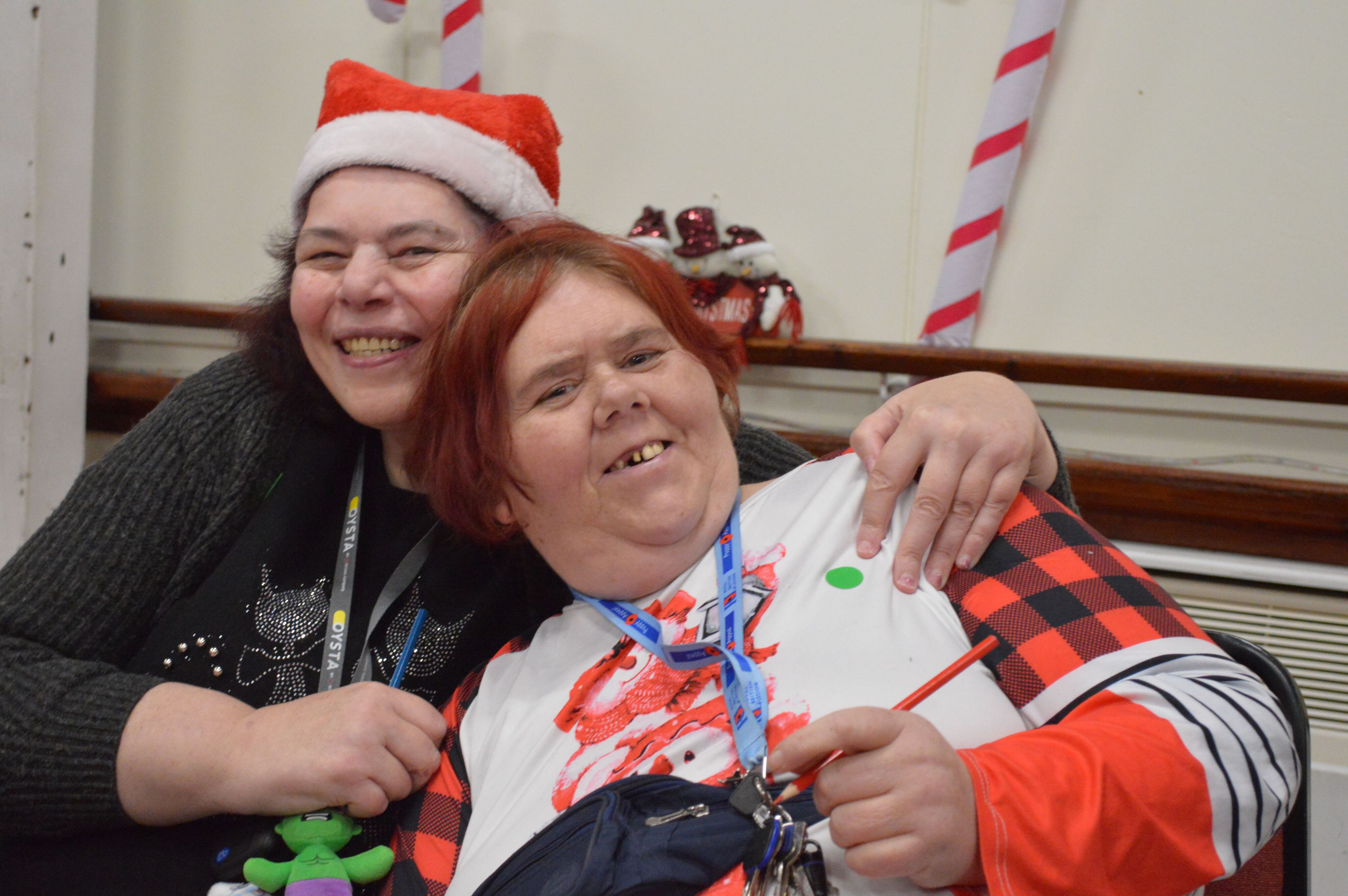Two people embracing, one wearing a Santa hat and the other in a red, sharing a festive moment indoors.