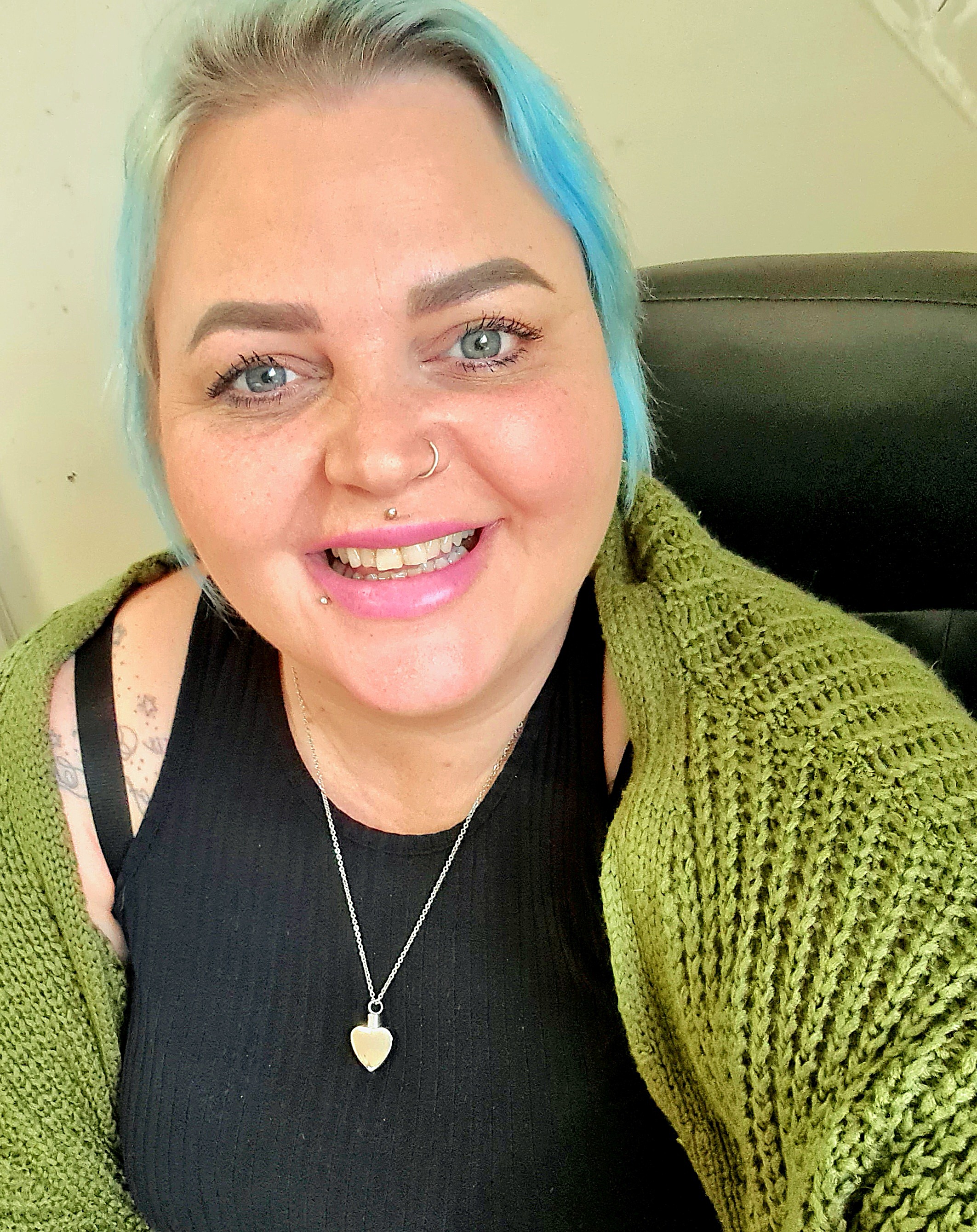 Melanie Fisher smiles at the camera with colourful blue hair and a silver heart necklace.