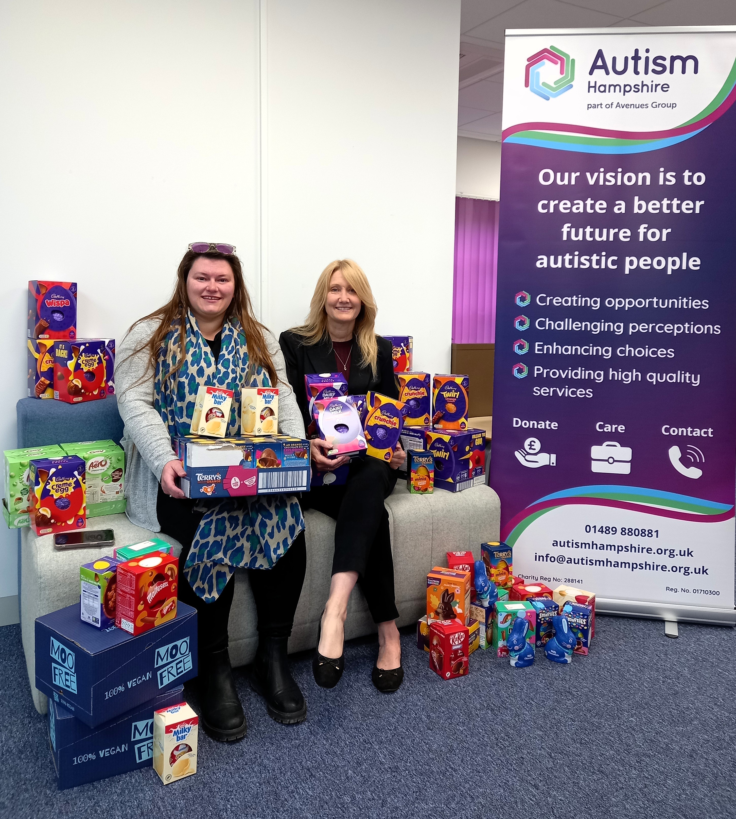Colleagues from Autism Hampshire and AECOM sit on a chair surrounded by Easter eggs.