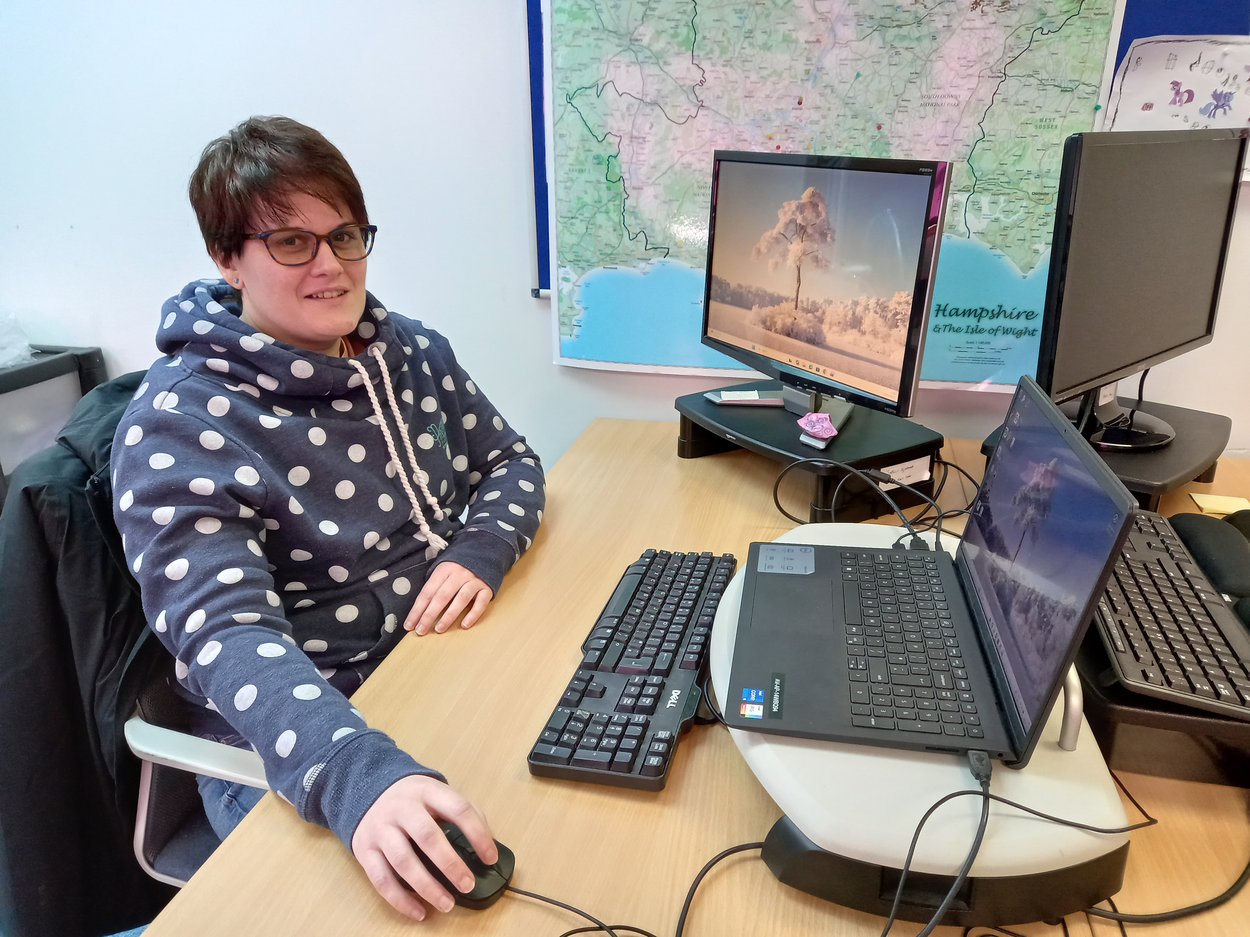 Sam sits at her desk with a laptop and map in the background.