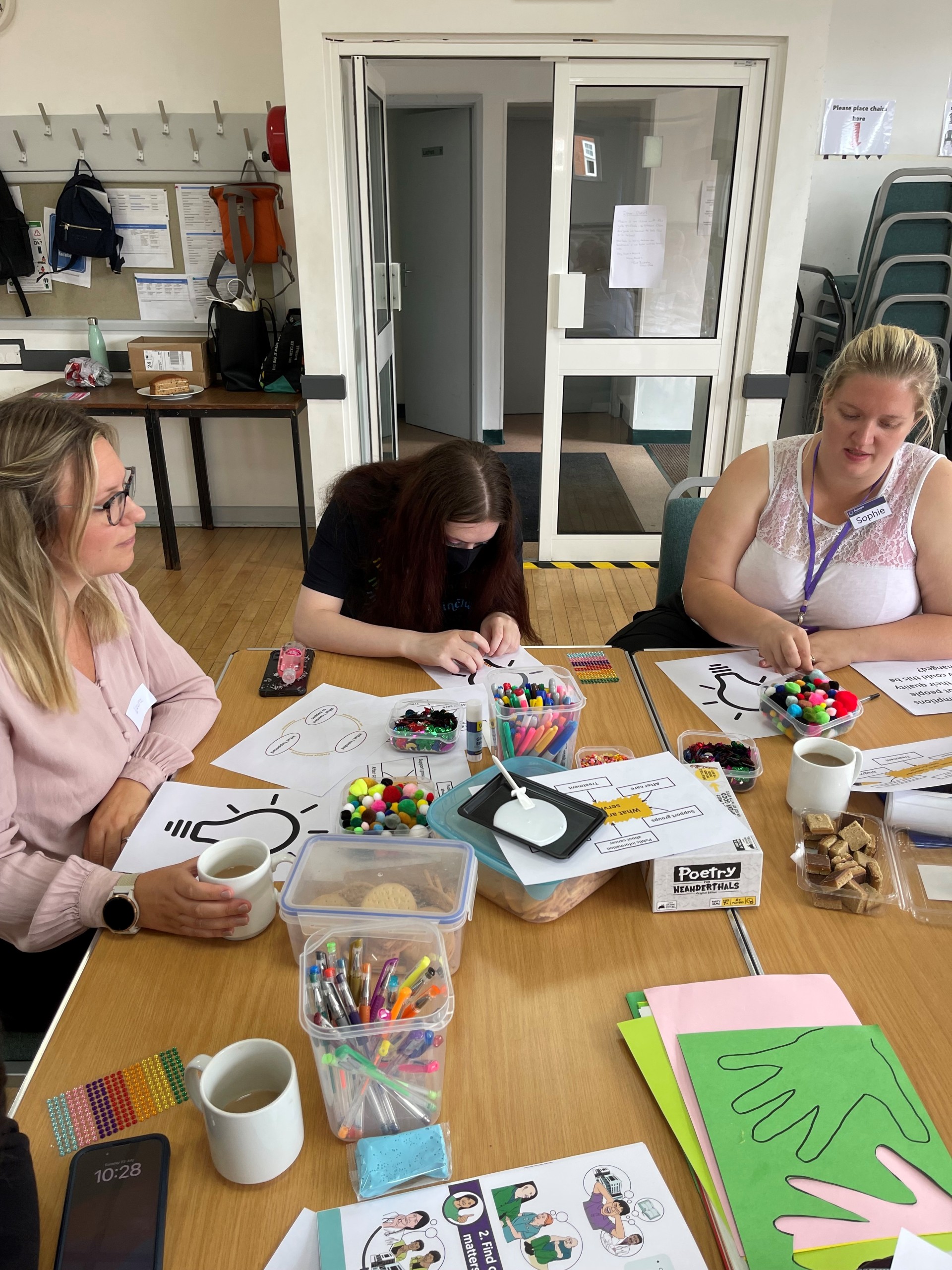 Three people sit at a table surrounded by craft materials.