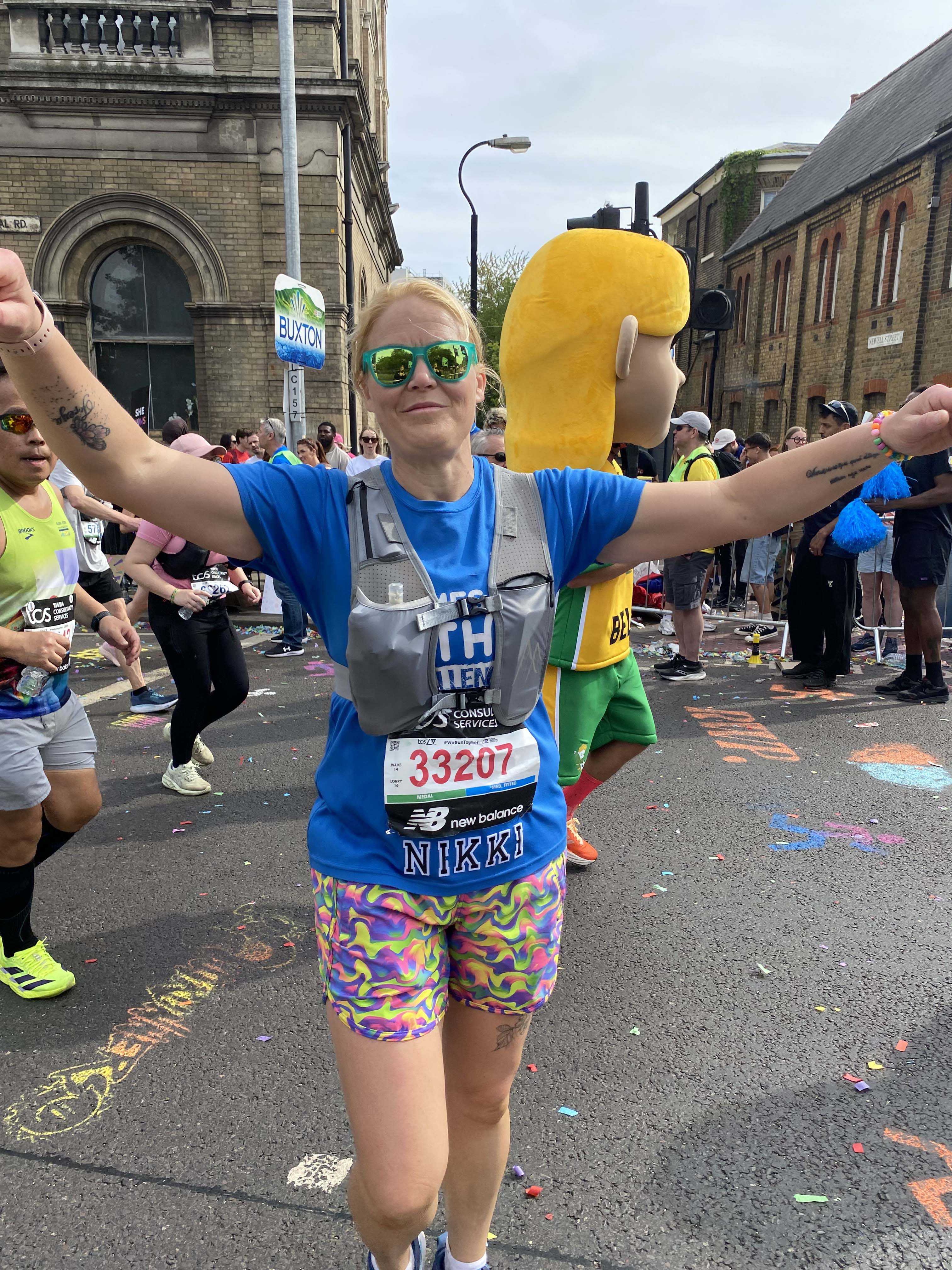 A lady in a blue vest with her arms in the air as she finishes the London marathon