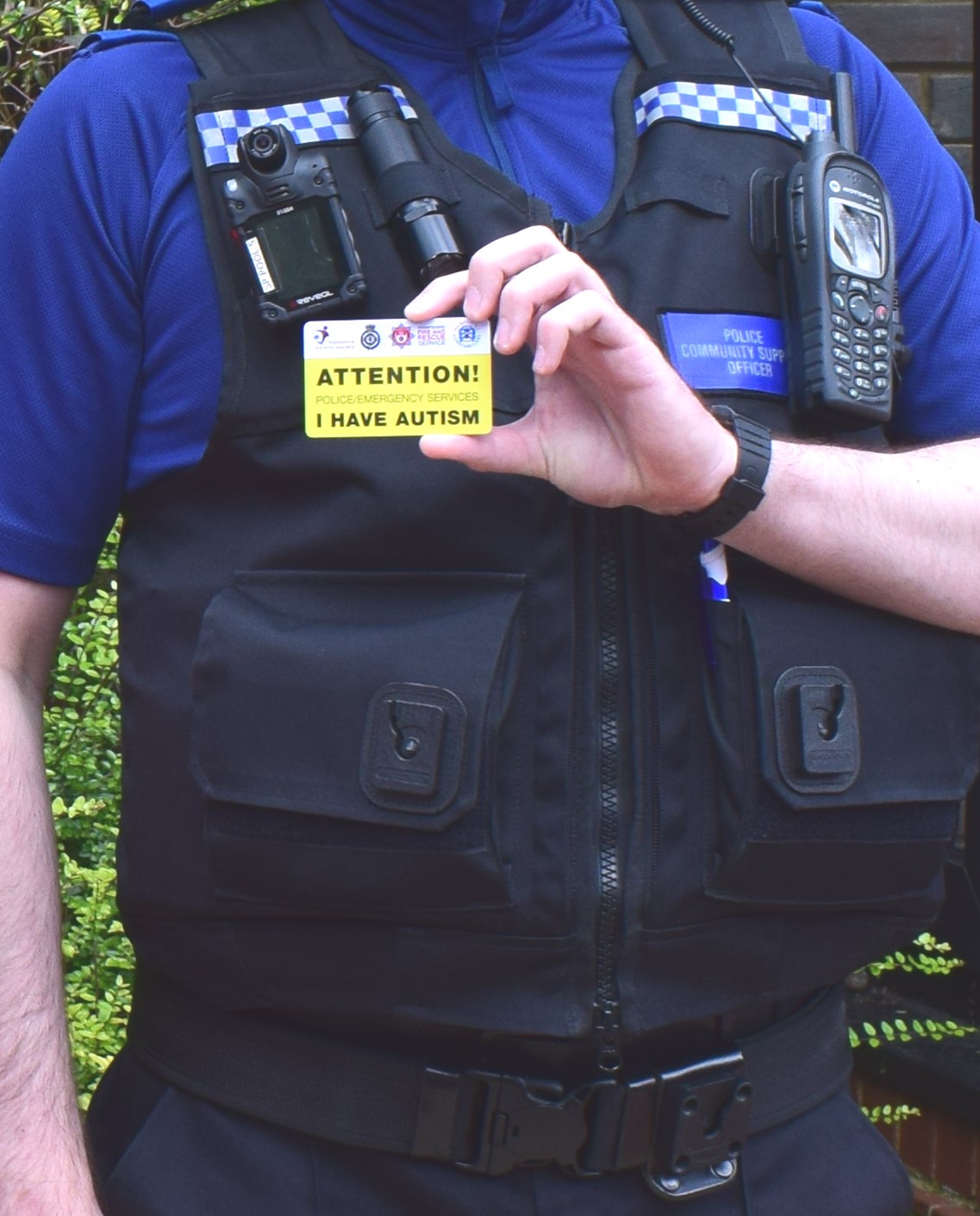 Police officer holding an autism alert card. It is yellow stating Attention, police/emergency services, I have autism.